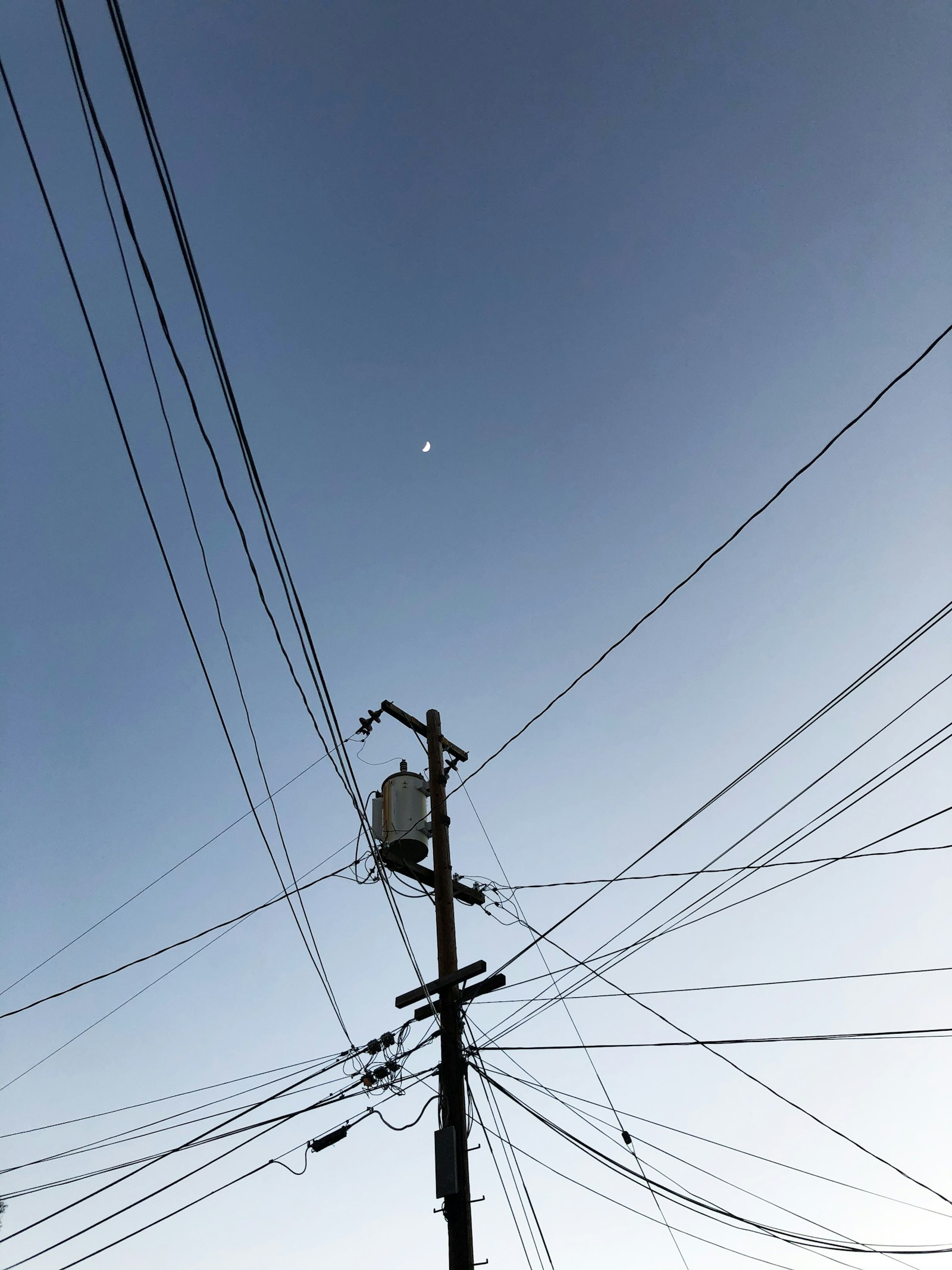 A telephone pole strung with overhead copper lines against a blue sky